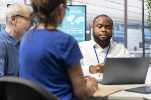 Male managed detection and response consultant helps two other people by showing them info on a laptop