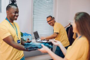 nonprofit volunteers sorting donated clothing while a staff member works on a laptop